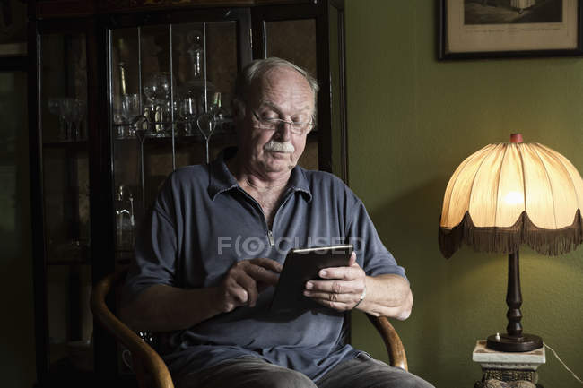 Hombre mayor usando mini tableta en casa - foto de stock