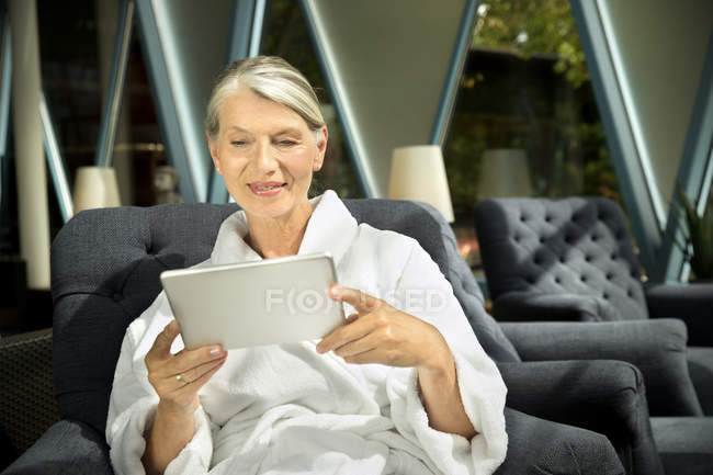Senior mulher de roupão sentado em poltrona usando tablet digital — Fotografia de Stock