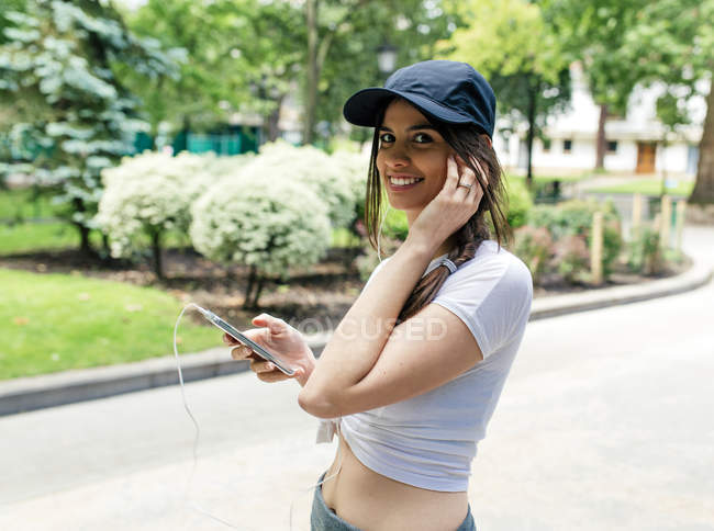 Портрет улыбающейся молодой женщины, слушающей музыку с наушниками в парке — стоковое фото