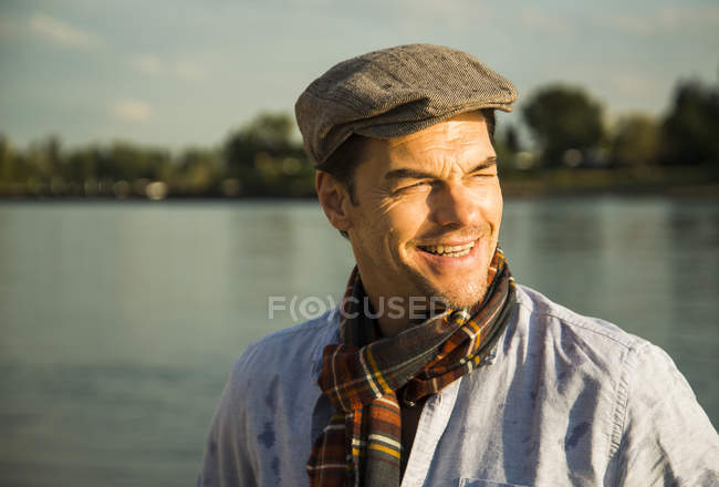 Retrato de um homem sorridente usando boné em frente a um rio ao entardecer — Fotografia de Stock