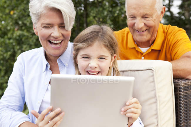 Heureux grands-parents et fille à l'extérieur en utilisant une tablette numérique — Photo de stock