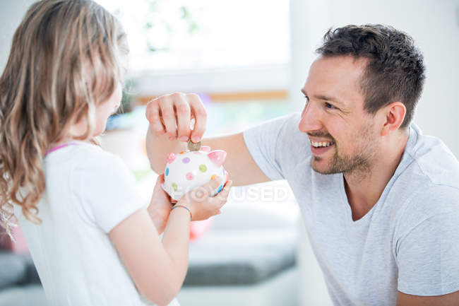 Vater und Tochter werfen zu Hause Münze in Sparschwein — Stockfoto