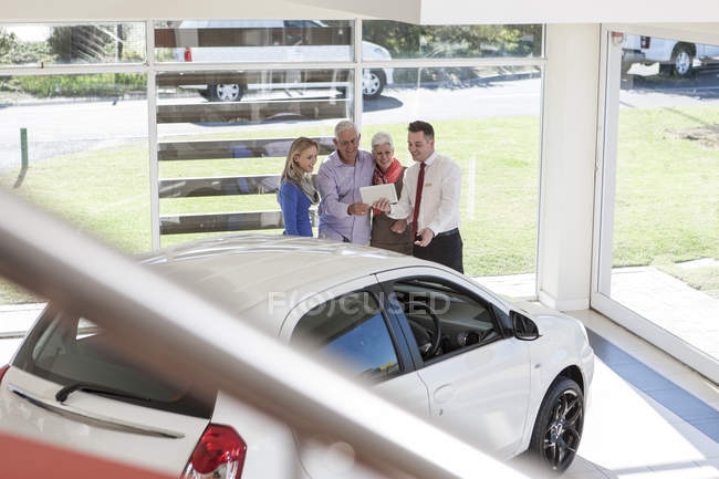 Clientes en concesionario de coches mirando tableta digital - foto de stock