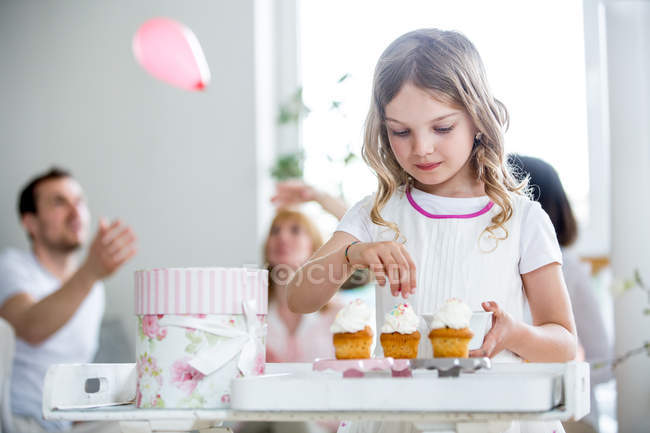 Menina enfeite bolos copo, família celebrando no fundo — Fotografia de Stock