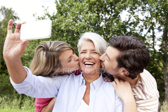 Glückliche Mutter mit erwachsenen Kindern beim Handy-Foto im Freien — Stockfoto