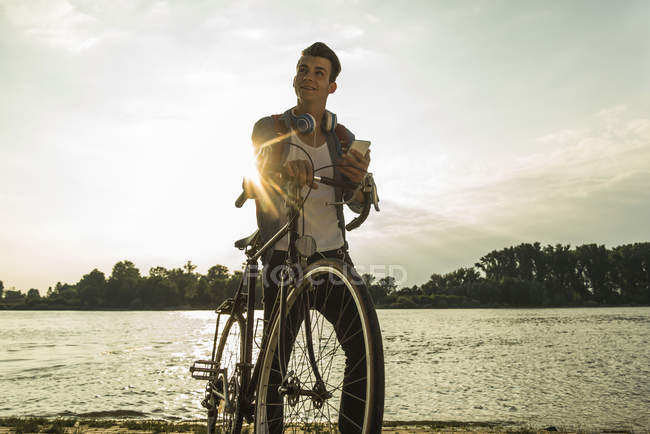 Giovane con bicicletta e cellulare sul lungofiume — Foto stock