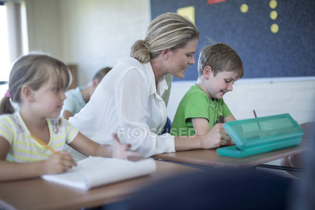 Teacher helping schoolboy in classroom at school — Stock Photo