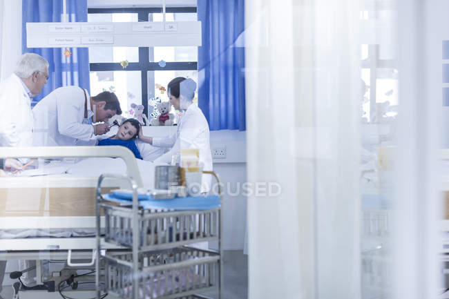 Лікарі, вивчаючи маленький хлопчик в лікарняному ліжку — стокове фото