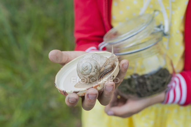 Menina segurando caracol na tampa e frasco de vidro — Fotografia de Stock