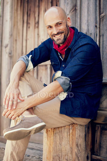 Ritratto di uomo sorridente seduto davanti a una capanna di legno — Foto stock