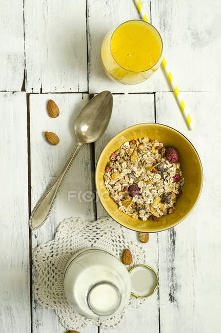 Bol de muesli aux fruits, verre de smoothie à la mangue, cuillère et bouteille de lait — Photo de stock