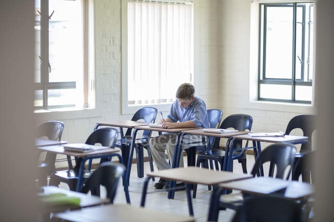 Schoolboy writing in classroom at school — Stock Photo