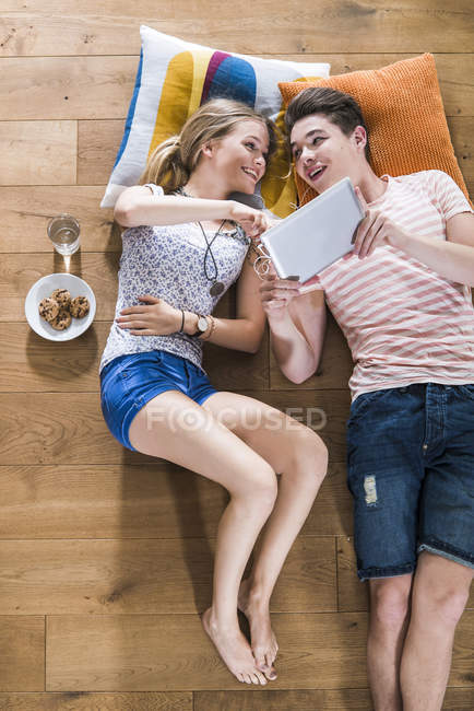 Happy Young Couple Lying On Floor Sharing Digital Tablet