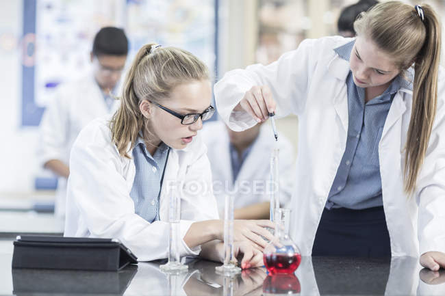 Dos colegialas en clase de química trabajando con líquidos - foto de stock