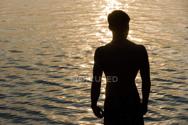 Silhueta de adolescente na frente de um lago no backlight — Fotografia de Stock