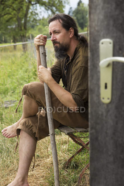 Hombre sentado con bastón de senderismo en cabaña de madera - foto de stock