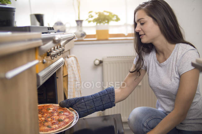 Donna che tira fuori la pizza dal forno — Foto stock