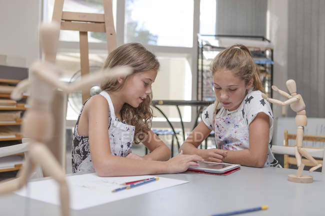 Two girls using digital tablet in an art class sitting at table — Stock Photo