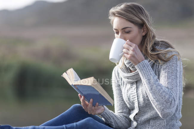 Mulher com livro beber café em um molhe no lago — Fotografia de Stock