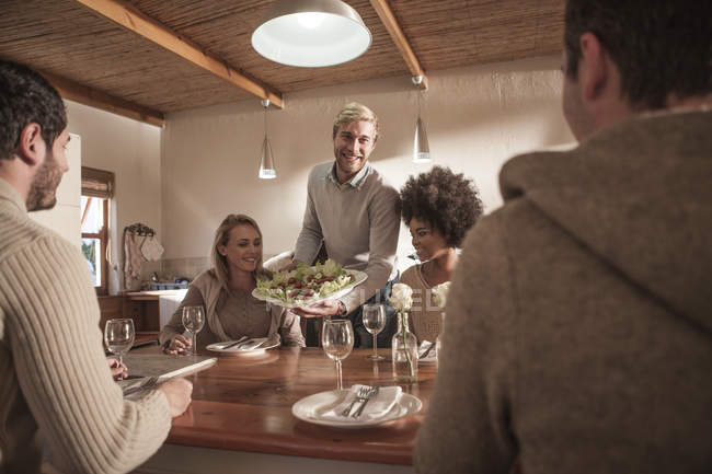 Young man serving plate with salad for friends — Stock Photo