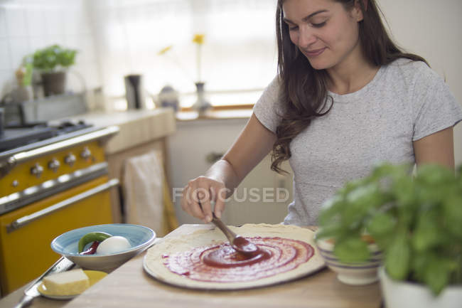 Young woman spreading tomato sauce on pizza dough — Stock Photo