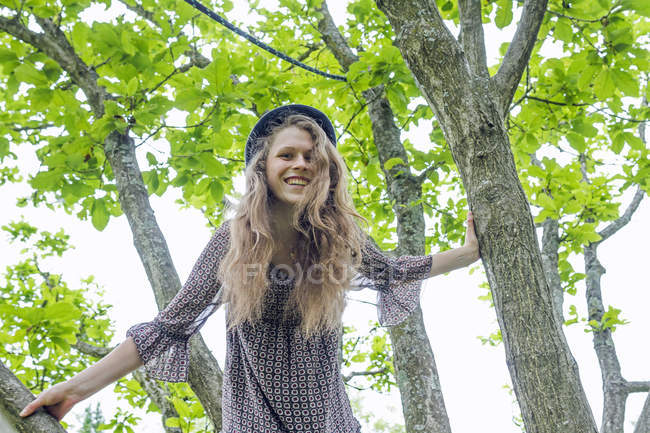 Портрет улыбающейся молодой женщины, взбирающейся на дерево — стоковое фото