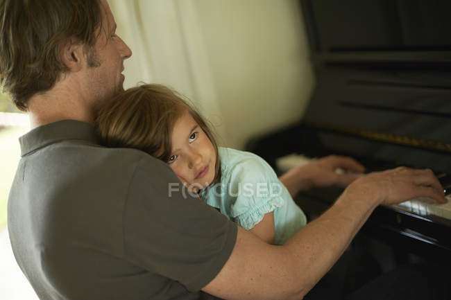 Father playing piano with daughter on his lap — Stock Photo