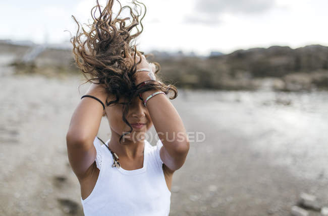 Little girl on the beach holding her blowing hair — Stock Photo