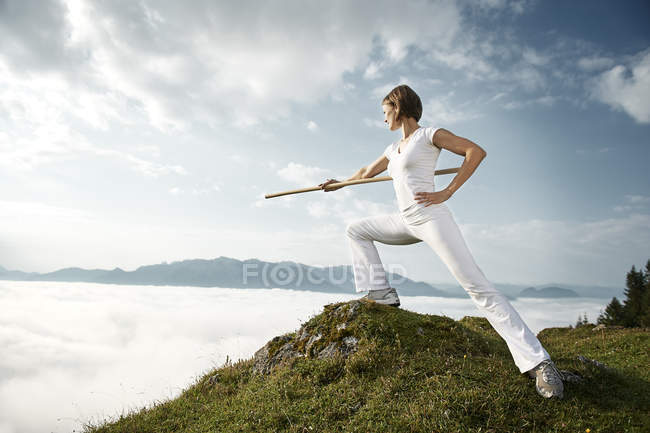 Austria, Kranzhorn, Mid adult woman exercising with fighting stick  on mountain top — Stock Photo