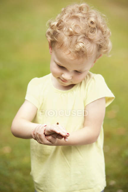 Kleines Mädchen beobachtet Marienkäfer auf ihrer Hand — Stockfoto