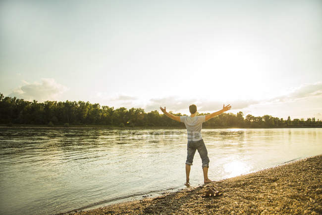 Vista posteriore dell'uomo in piedi lungo il fiume con le braccia tese — Foto stock