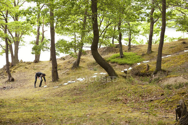 Hombre de negocios recogiendo hojas de papel del suelo forestal - foto de stock