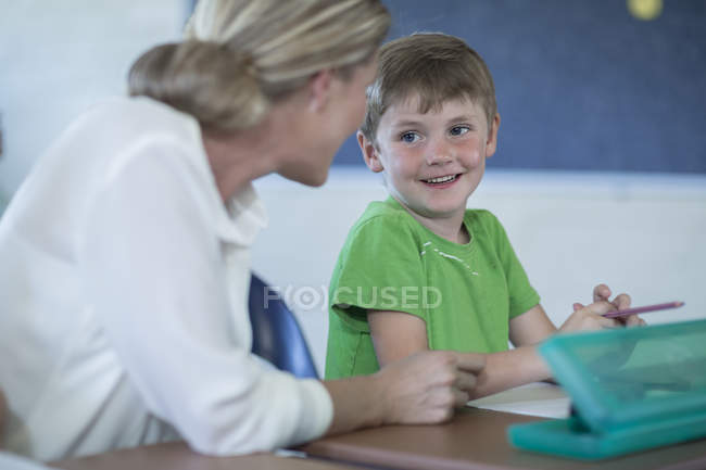 Smiling teacher and schoolboy talking in classroom — Stock Photo