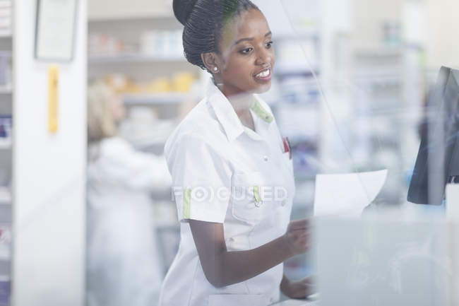 Аптекарь держит рецепт стоя за стеклом — стоковое фото