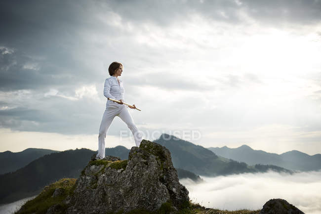 Austria, Kranzhorn, Mujer adulta haciendo ejercicio con palo de lucha en la cima de la montaña - foto de stock