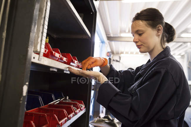 Giovane donna che lavora in garage di riparazione, alla ricerca di pezzi di ricambio — Foto stock