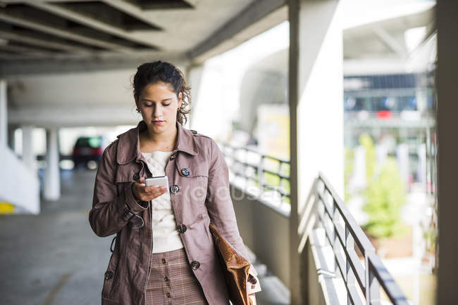 Mujer joven utilizando el teléfono inteligente en el aparcamiento - foto de stock