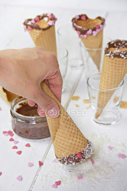 Ice-cream cones with chocolate, sugar hearts and hand dipping cone in coconut flakes — Stock Photo