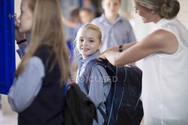 Teacher helping schoolgirl with backpack on hallway — Stock Photo