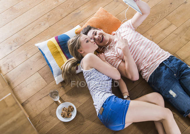 Happy young couple lying on floor sharing digital tablet — Stock Photo