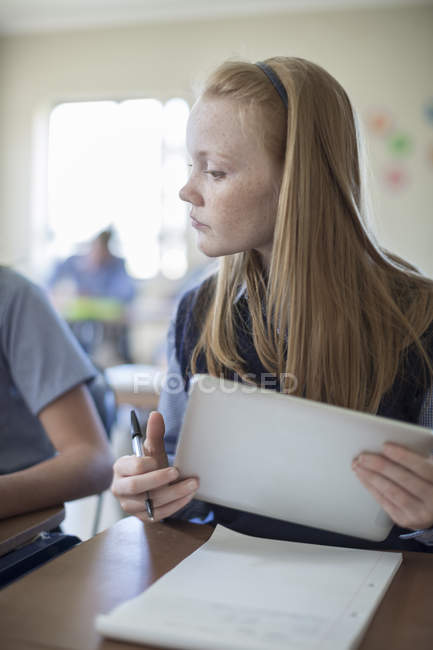 Schoolgirl in classroom with digital tablet looking to classmate — Stock Photo