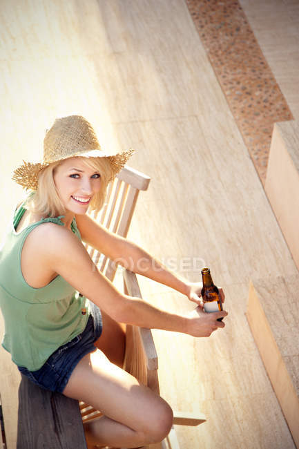 Усміхнена молода жінка п'є пиво на терасі — стокове фото
