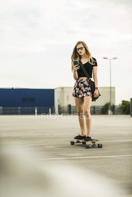 Девушка-подросток катается на скейтборде и смотрит на мобильный телефон — стоковое фото