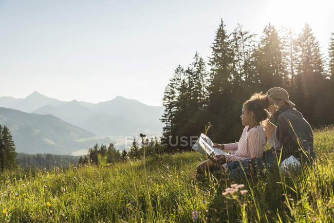 Austria, Tirol, Tannheimer Tal, pareja joven descansando en el prado alpino mirando el mapa - foto de stock