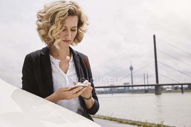 Junge Frau schreibt SMS am Flussufer — Stockfoto