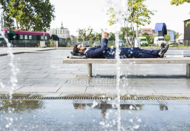 Молодой бизнесмен лежит на скамейке, работает — стоковое фото