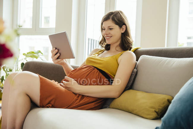 Вагітна жінка з цифровим планшетом розслабляється на дивані вдома — стокове фото