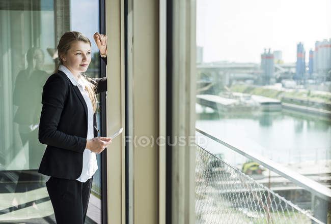 Giovane donna d'affari con tablet digitale guardando fuori dalla finestra — Foto stock