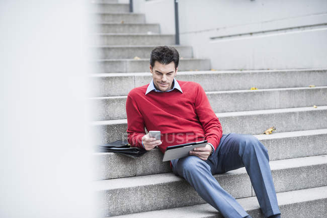 Geschäftsmann mit digitalem Tablet und Smartphone sitzt auf Treppe — Stockfoto