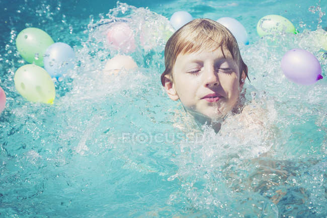 Boy in swimming pool surrounded by balloons — Stock Photo